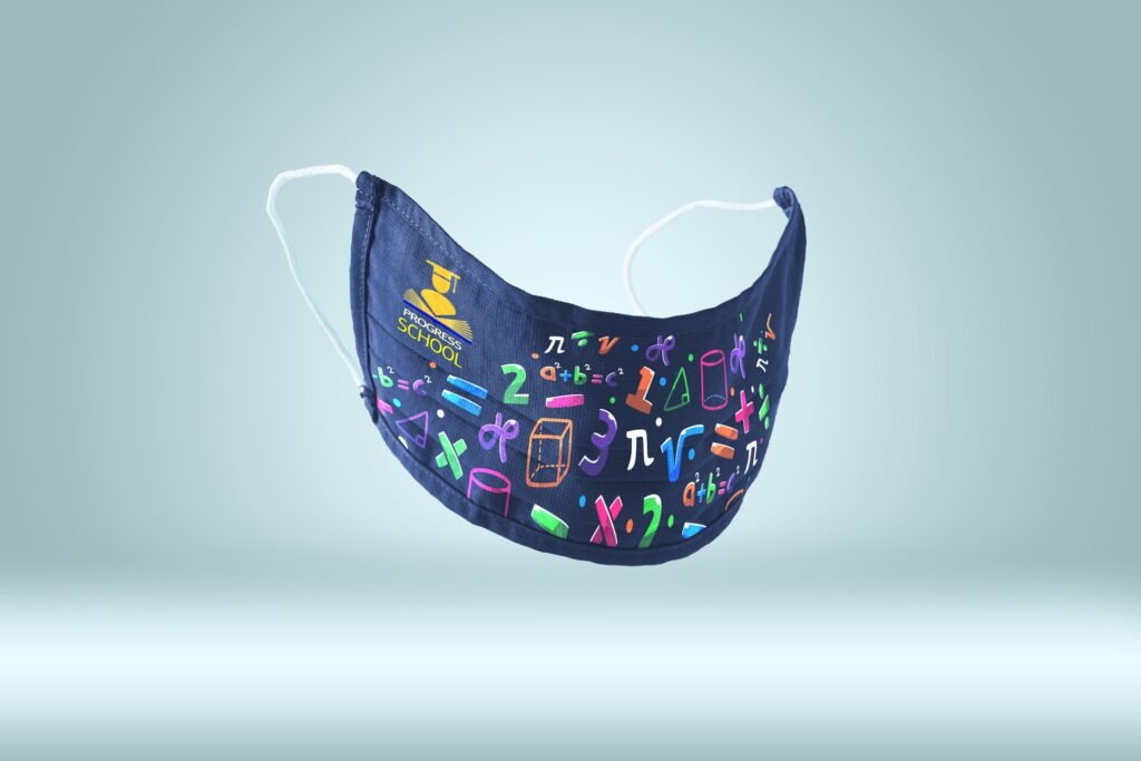Mascarilla azul oscuro con patrón de símbolos matemáticos coloridos y logo amarillo "PROGRESS SCHOOL" con birrete y libro.