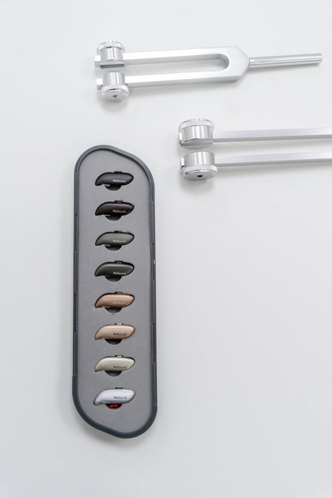 Estuche con 8 audífonos ReSound de varios colores y 3 diapasones plateados sobre fondo blanco.