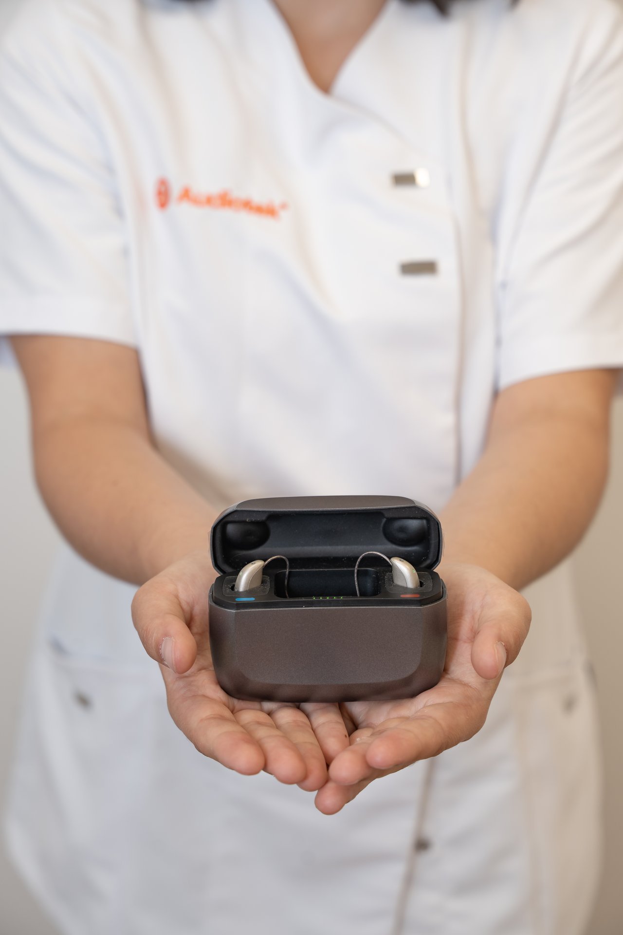 Persona con uniforme blanco sosteniendo estuche abierto con dos audífonos Audiotek dentro.