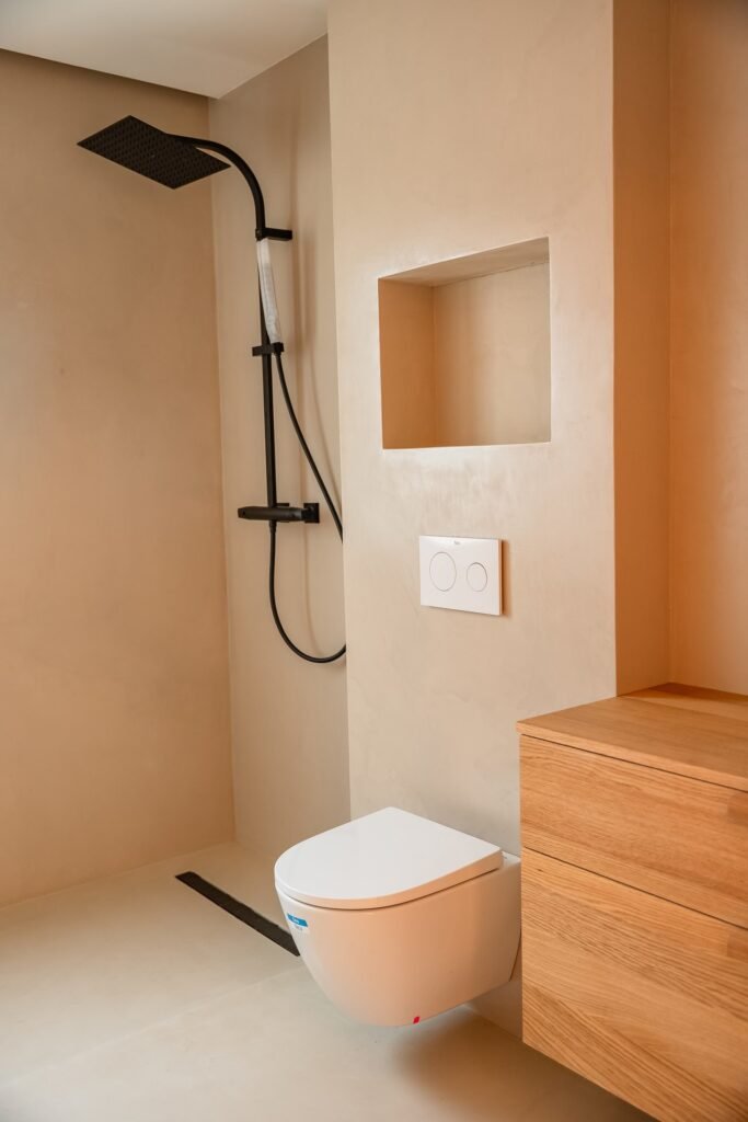 Baño moderno con ducha negra, inodoro suspendido blanco, mueble de madera y nicho en pared beige. Diseño minimalista.