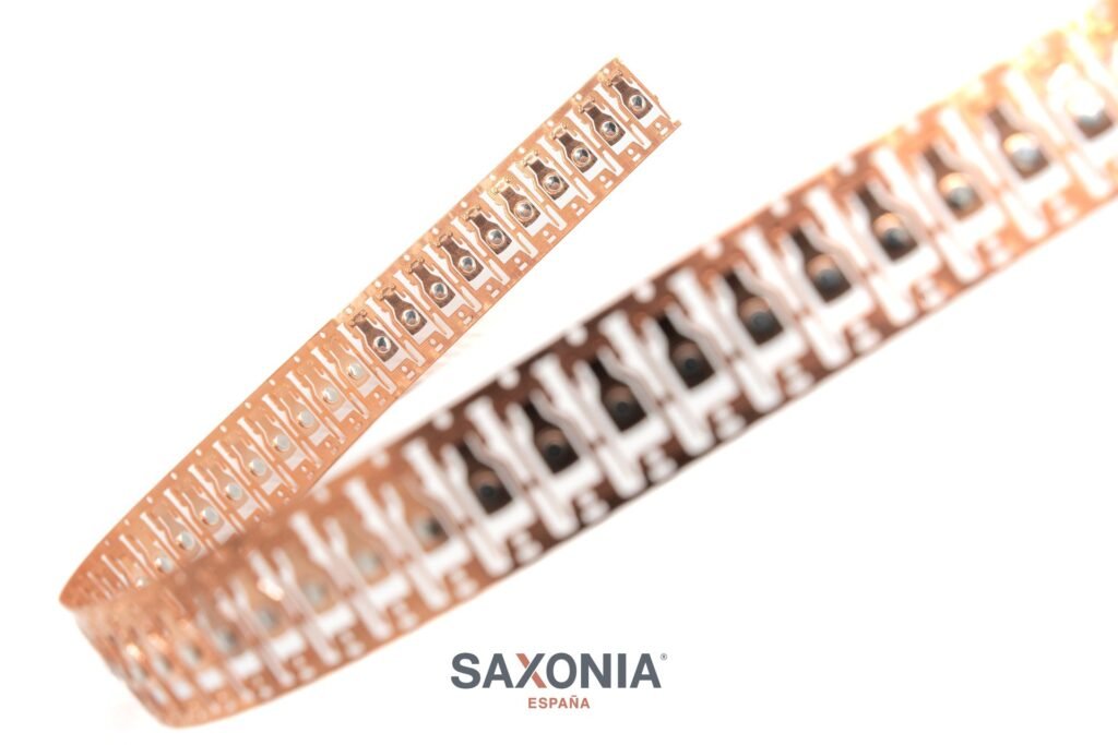 Tira de componentes electrónicos SAXONIA, color cobre con puntos metálicos, sobre fondo blanco.