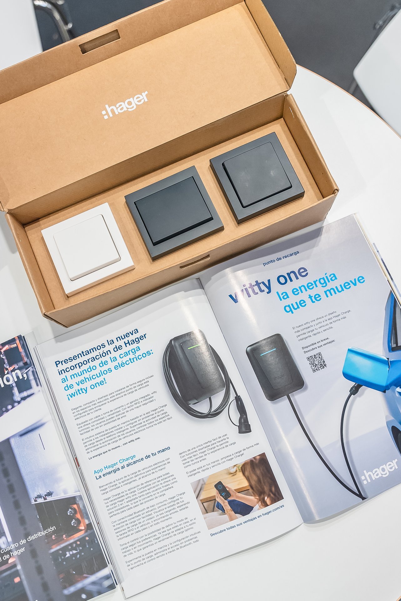Caja Hager con interruptores eléctricos (blanco, gris oscuro) y revista abierta sobre cargadores de vehículos eléctricos Witty One.