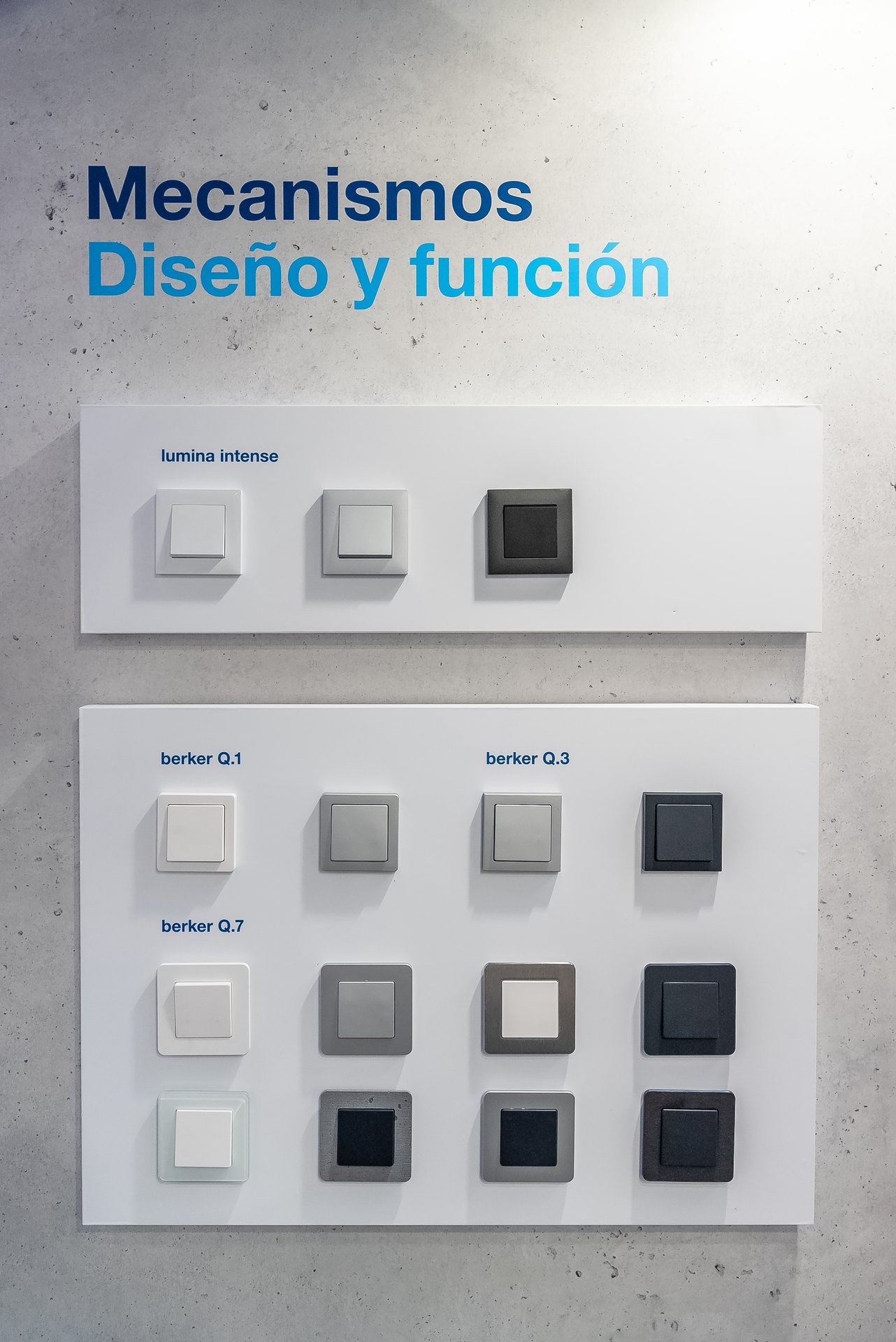 Exhibición de interruptores y mecanismos eléctricos en Efintec. Diversos modelos y acabados. Texto en pared: 'Mecanismos Diseño y función'.
