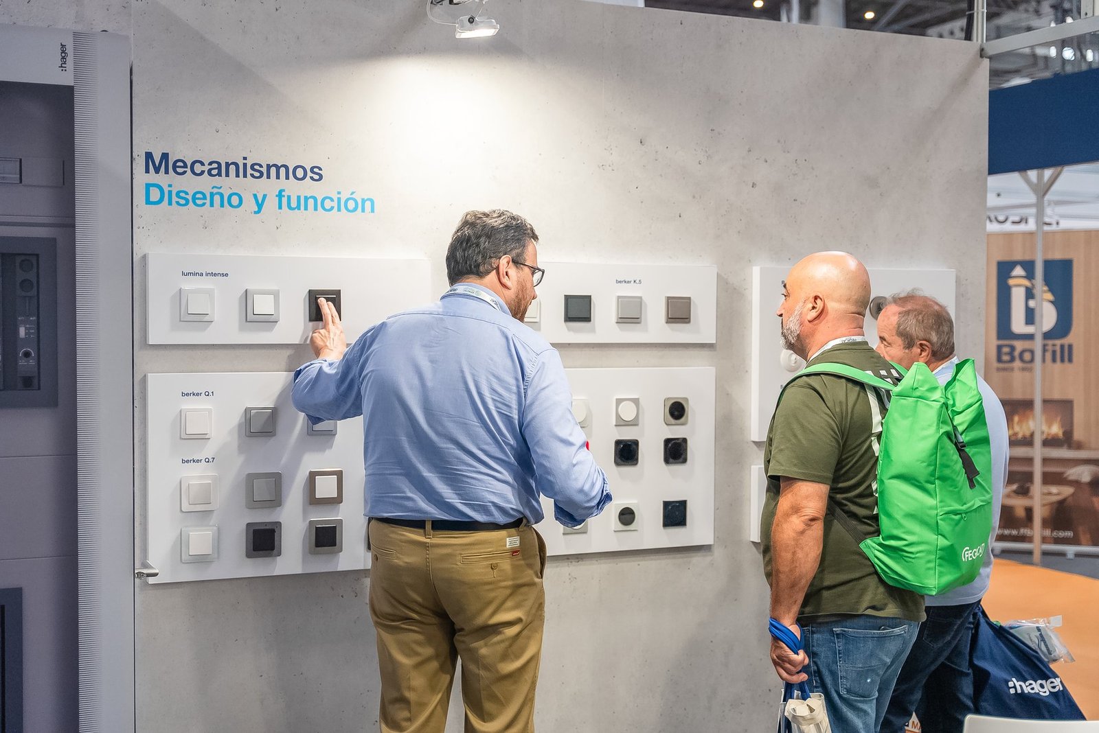 Hombre señalando mecanismos eléctricos en un stand de Efintec. Se ven interruptores y enchufes de varios diseños y colores.