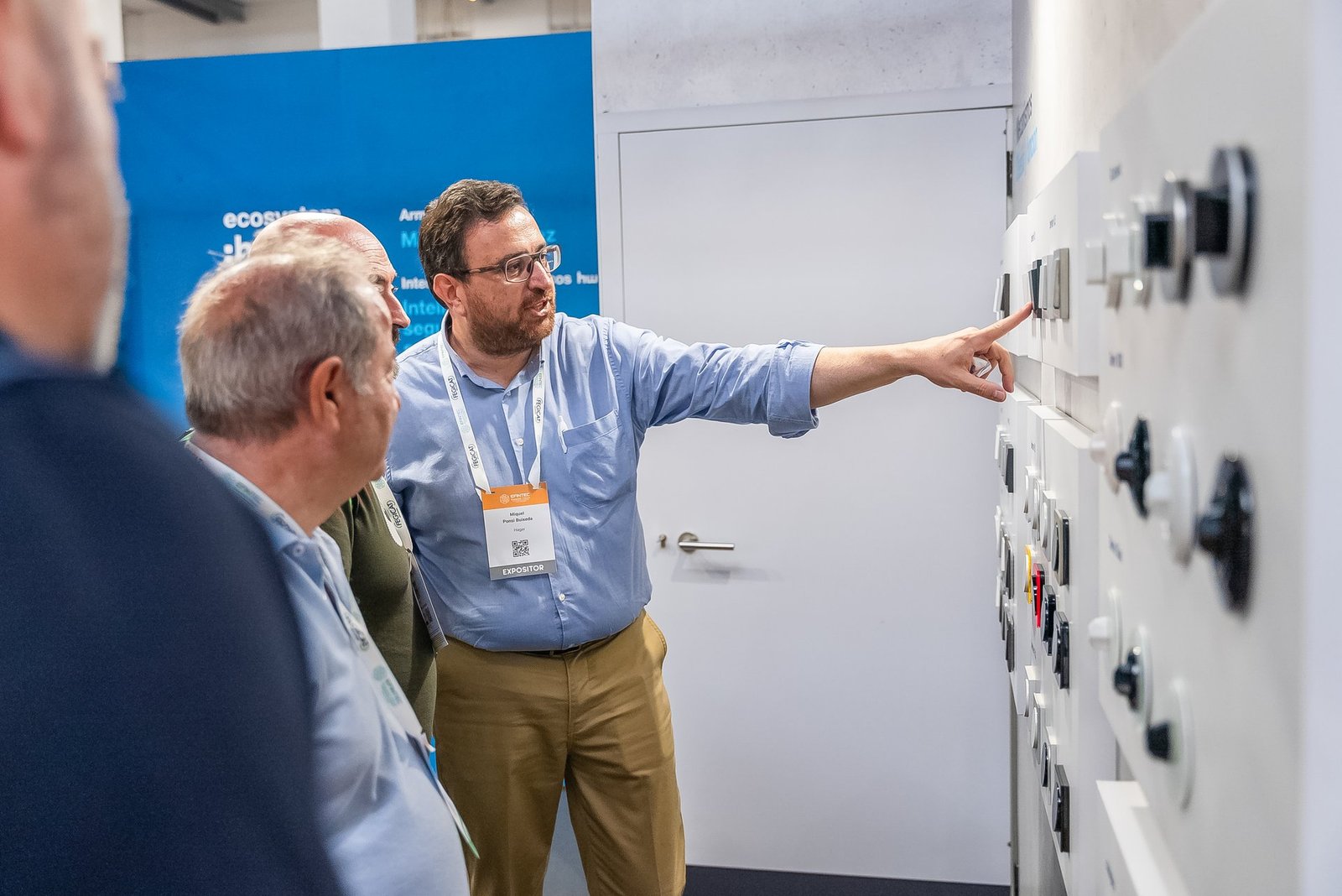 Expositor de Hager en Efintec explicando un panel de interruptores y controles eléctricos a dos asistentes.