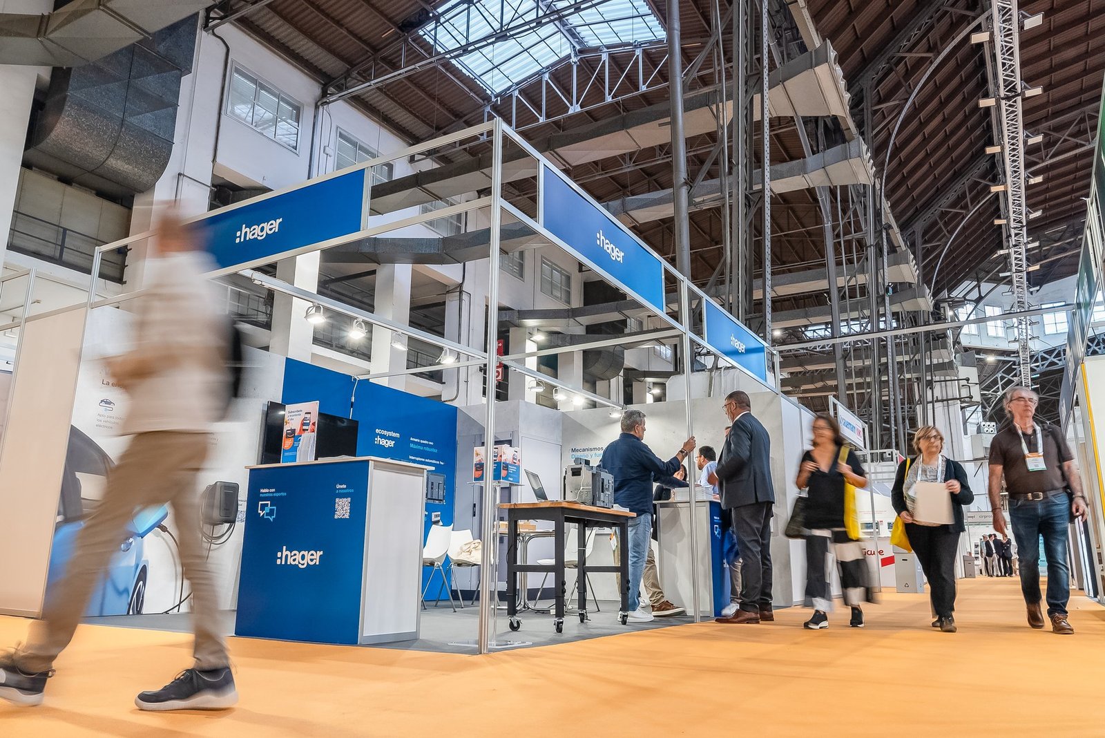 Stand de Hager en la feria Efintec. Personas interactúan con productos eléctricos y cargadores en un recinto industrial.