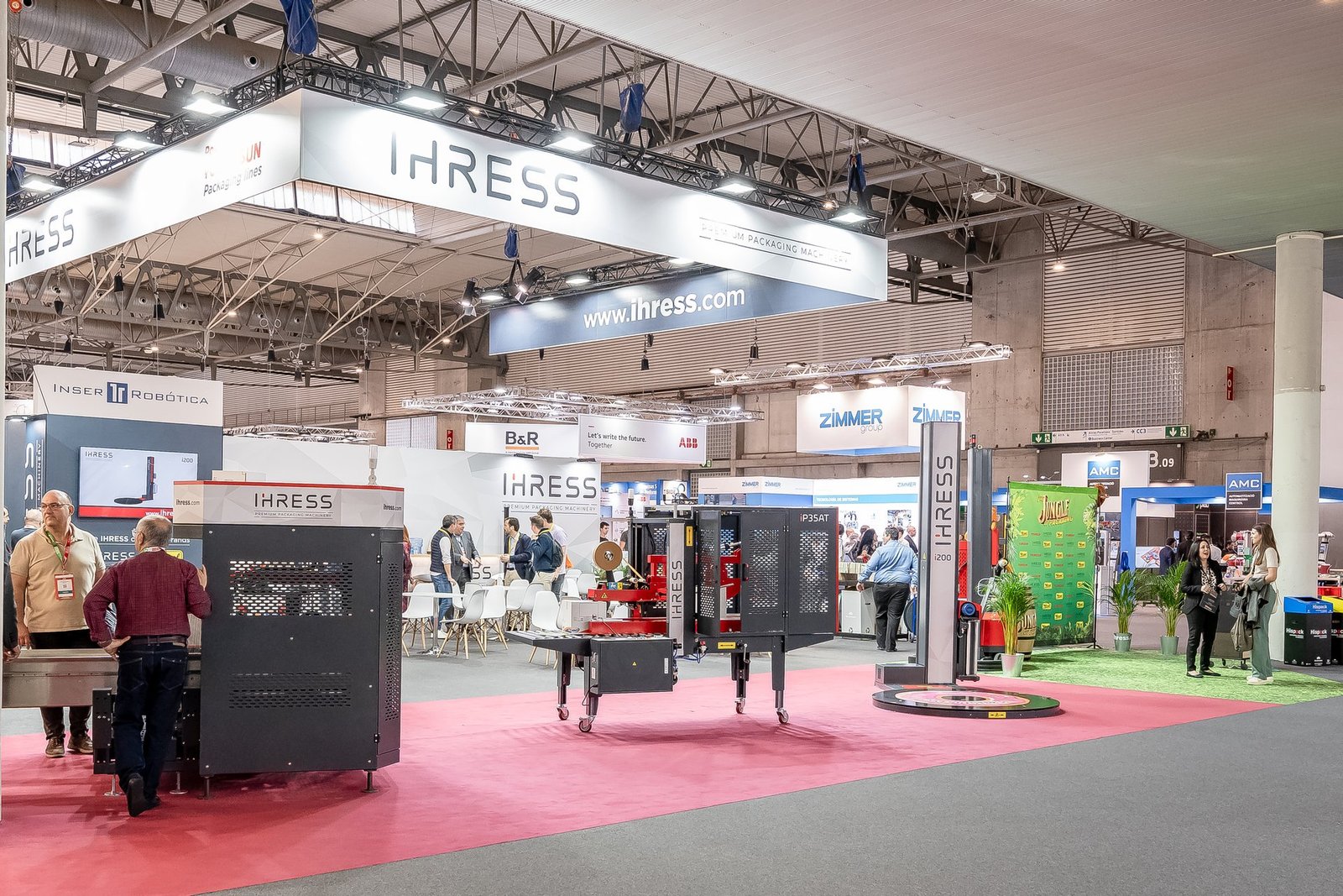Stand de IHRESS en Hispack con maquinaria de embalaje, banners de la marca y visitantes interactuando en la feria.