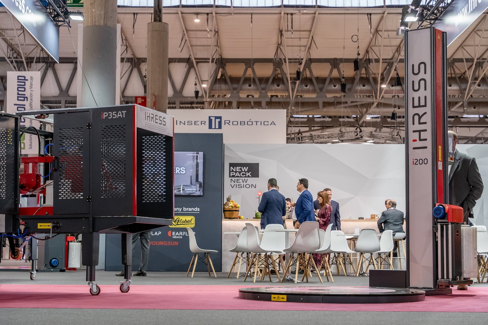 Stand IHRESS en Hispack: máquina iP3SAT, embaladora i200 y área de recepción con visitantes. Banners de Inser Robótica.