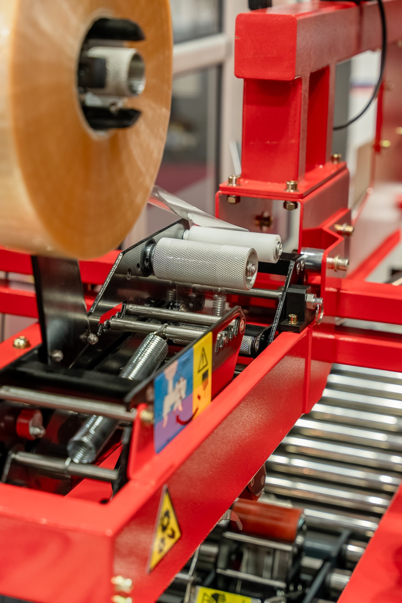Primer plano de máquina de embalaje roja en Hispack, con rollo de film transparente, rodillos y mecanismos.