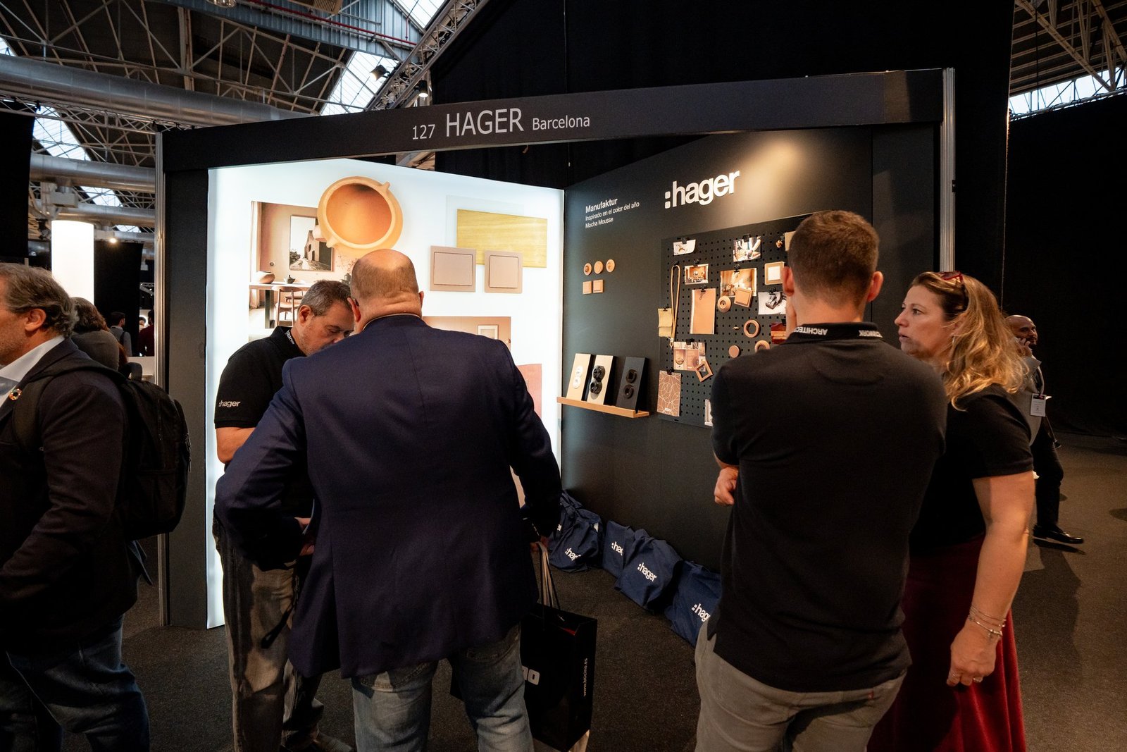 Visitantes interactúan en el stand de Hager en el evento Architect & Work. Se muestran productos eléctricos y diseños.