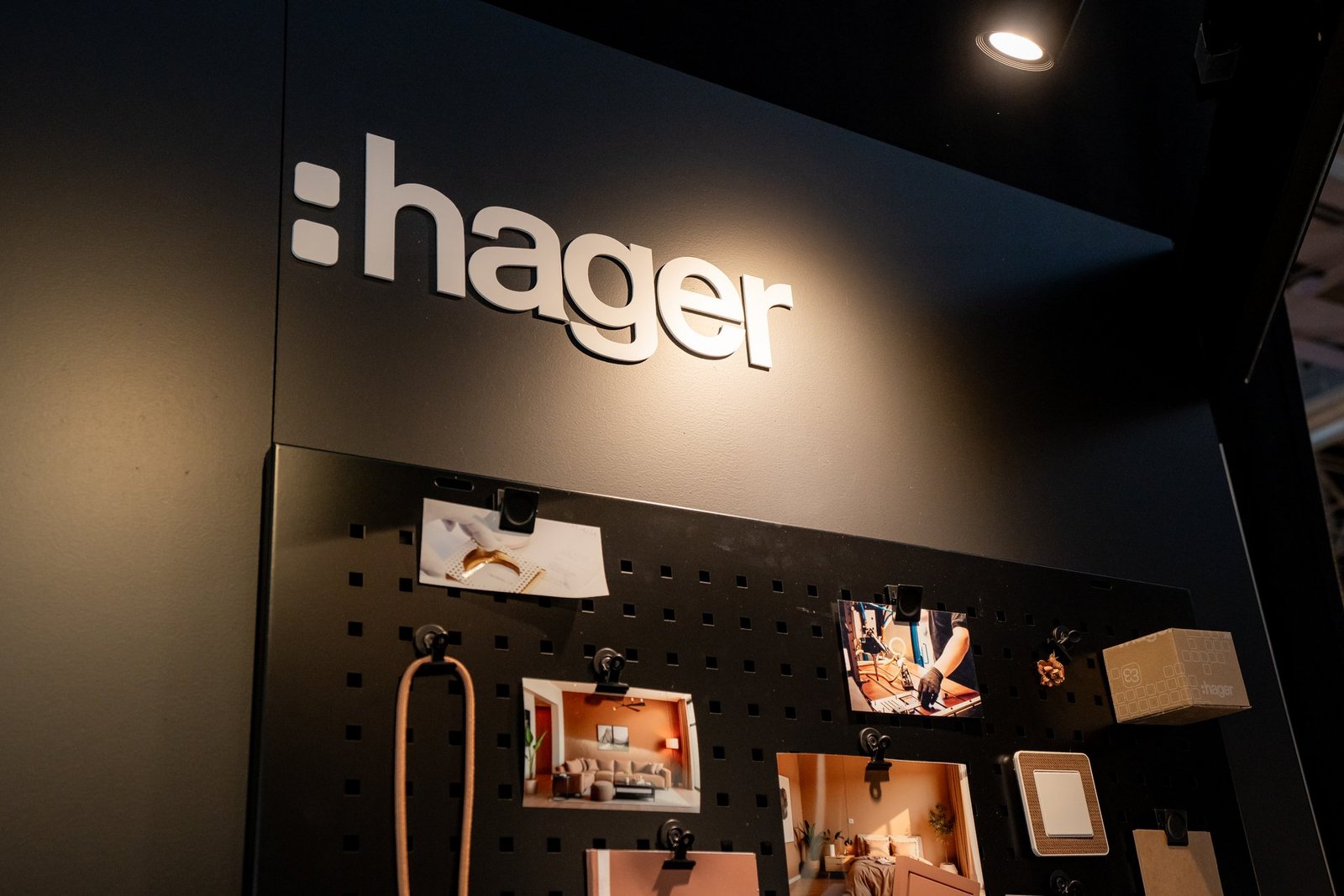 Logo blanco de Hager en pared negra. Panel con fotos de diseño interior, un interruptor y una caja de producto.