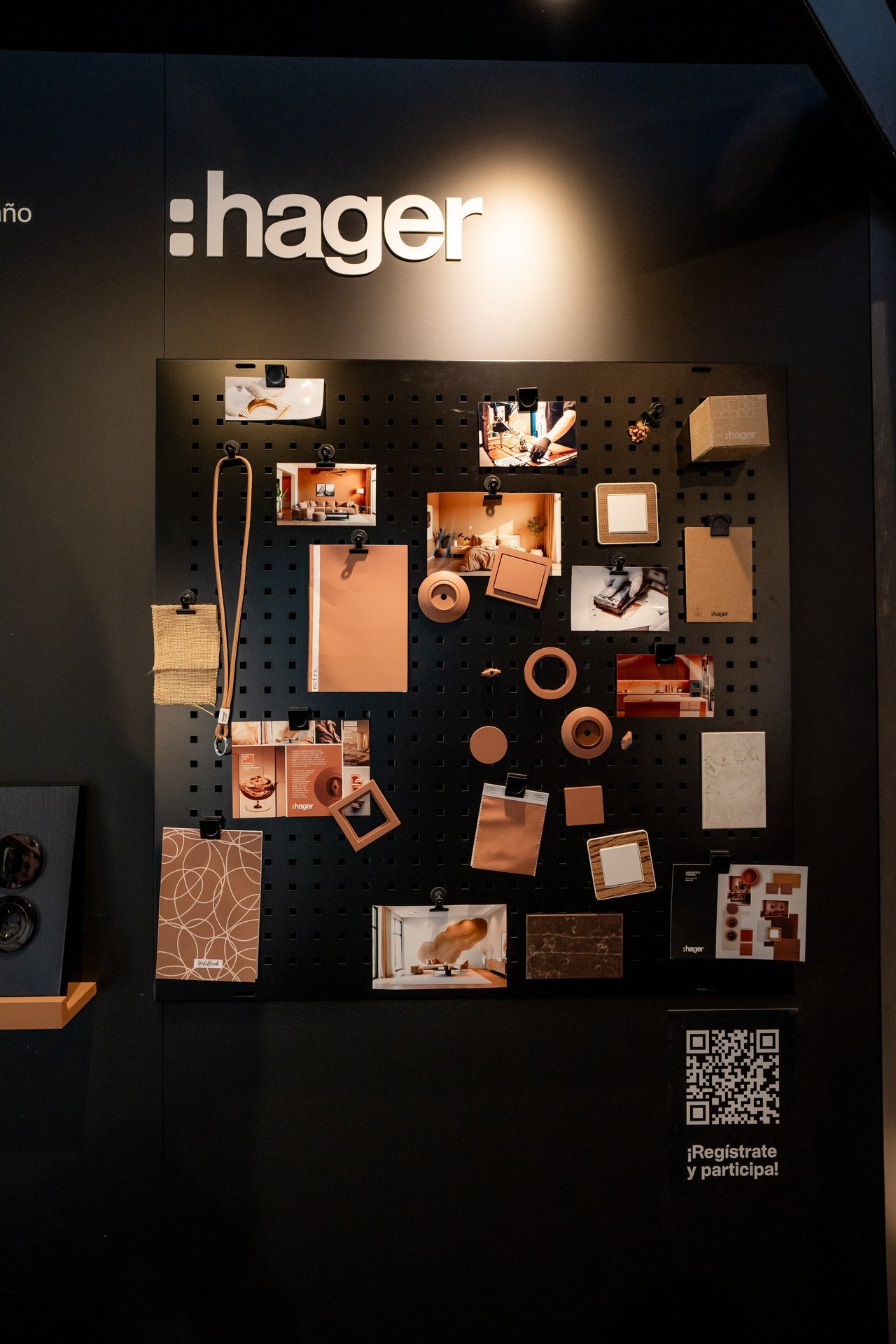 Panel expositor negro de Hager con muestras de productos, fotos de interiores y materiales en tonos cobre y blanco. Incluye QR para regis…