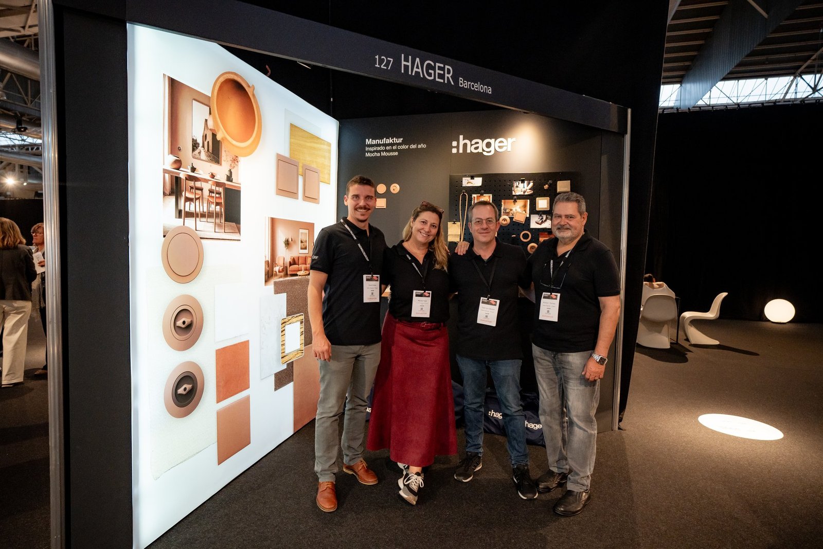 Cuatro miembros del equipo de Hager sonriendo frente a su stand en Architect & Work, mostrando paneles de diseño interior y productos elé…