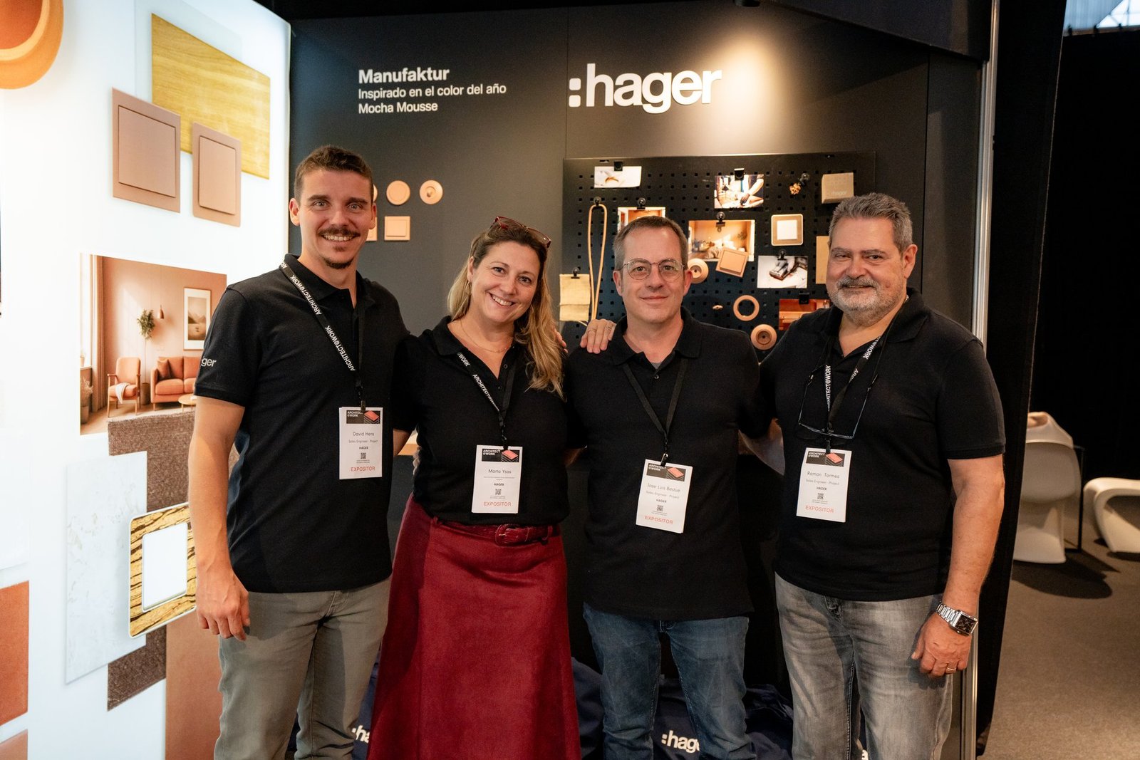 Cuatro miembros del equipo Hager sonriendo en su stand de Architect@Work, mostrando productos y soluciones.