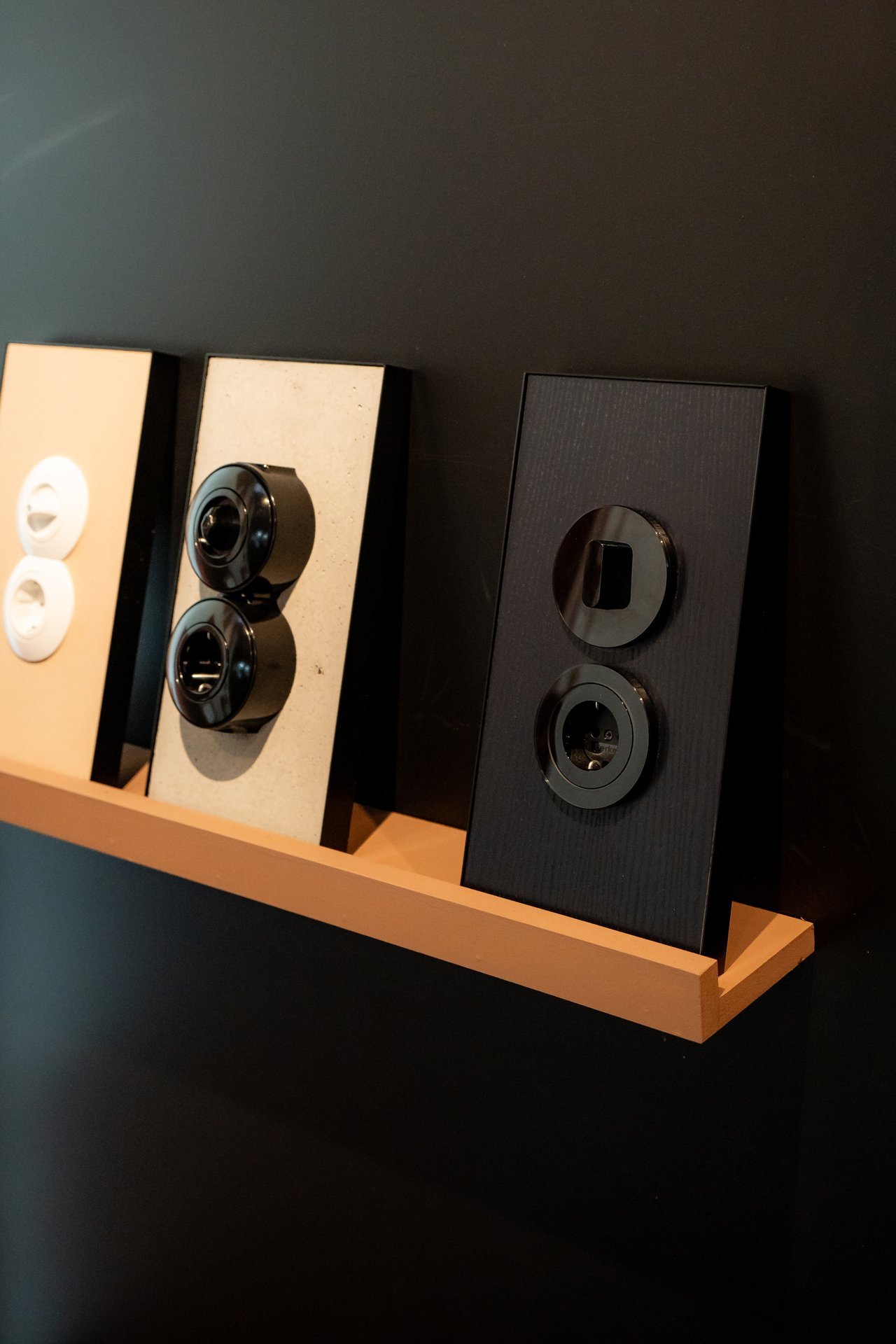Tres paneles exhiben interruptores y enchufes Hager: blancos en beige, negros en gris, y oscuros en negro texturizado.