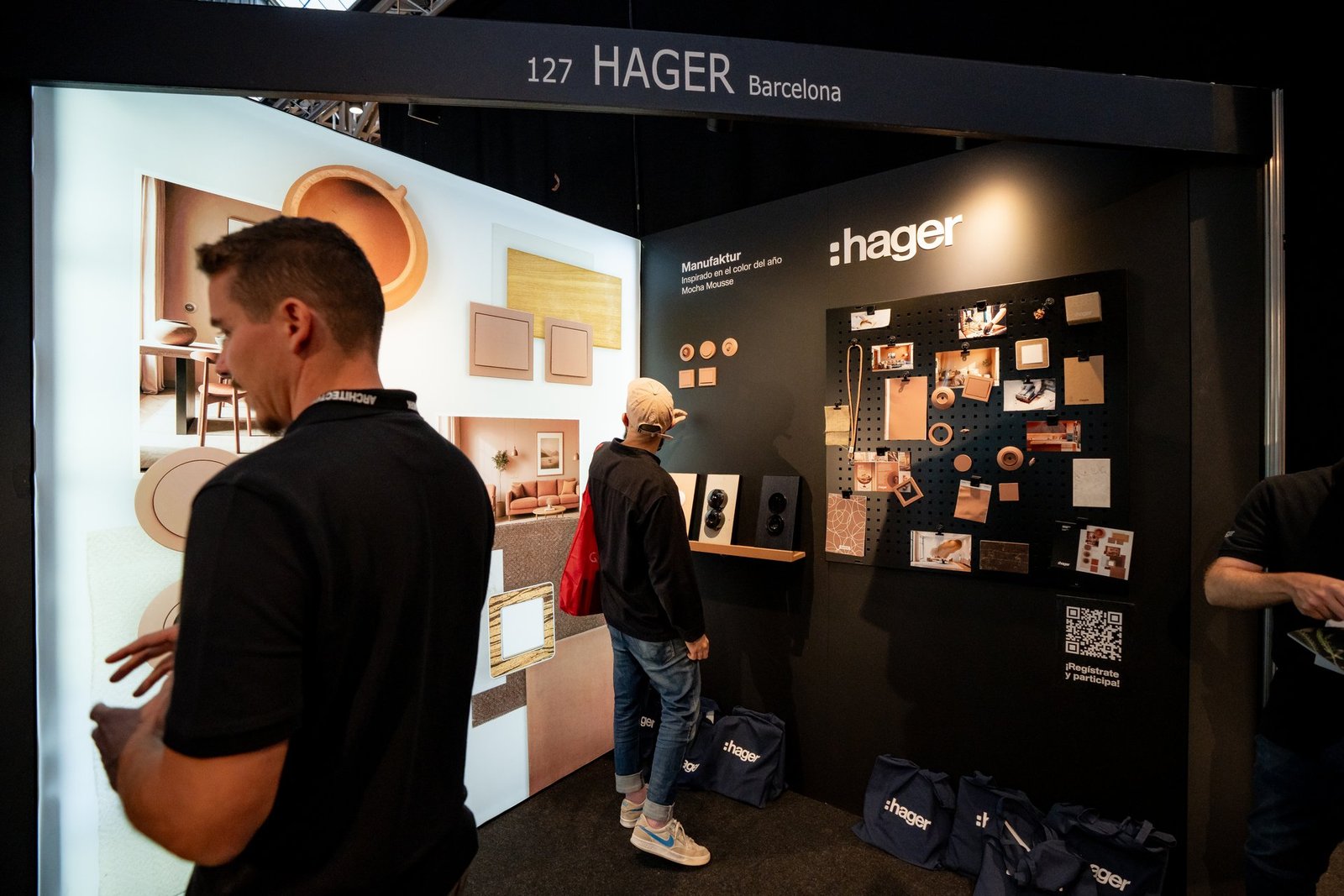 Stand Hager en Architect & Work. Dos personas ven expositores con interruptores, enchufes y muestras de diseño, incluyendo la colección M…