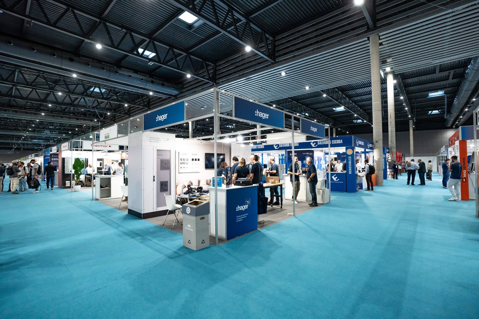 Stand principal de Hager en la feria Efintec, con personas interactuando. Gran sala de exposiciones con alfombra azul y otros stands.