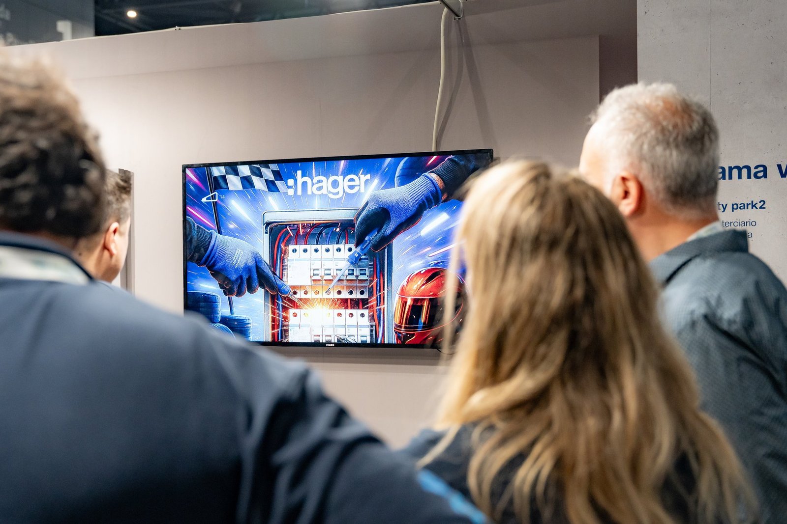 Público en Efintec observa pantalla Hager: manos enguantadas manipulan un panel eléctrico con chispas.