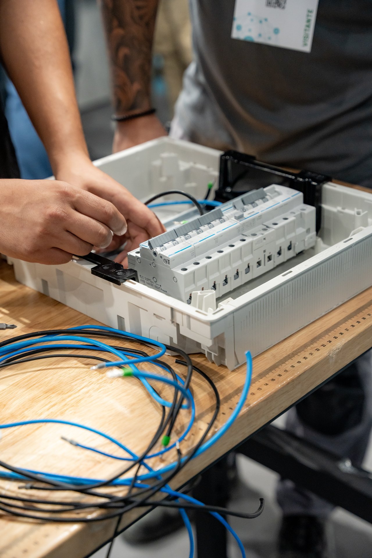 Manos conectando cables azules y negros a un cuadro eléctrico Hager con componentes modulares blancos. Evento Efintec.