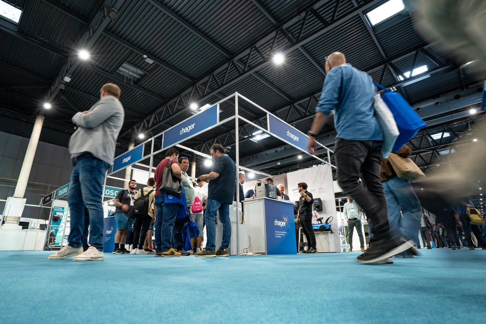 Visitantes en el stand de Hager en la feria Efintec. Varias personas interactúan y caminan por el pasillo con alfombra azul.