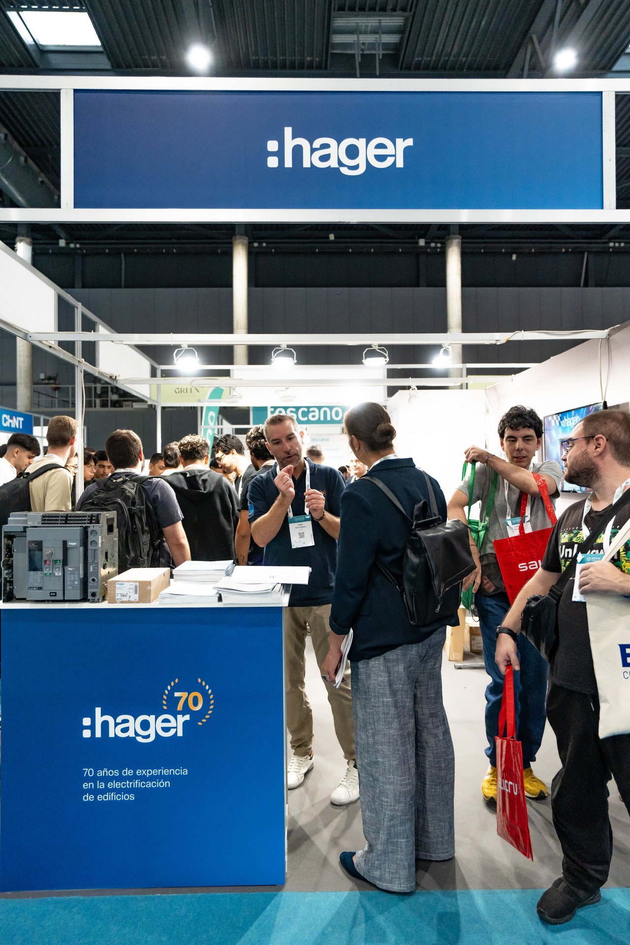 Stand de Hager en Efintec con personas interactuando. Se exhiben productos eléctricos y el logo de Hager con '70 años de experiencia'.
