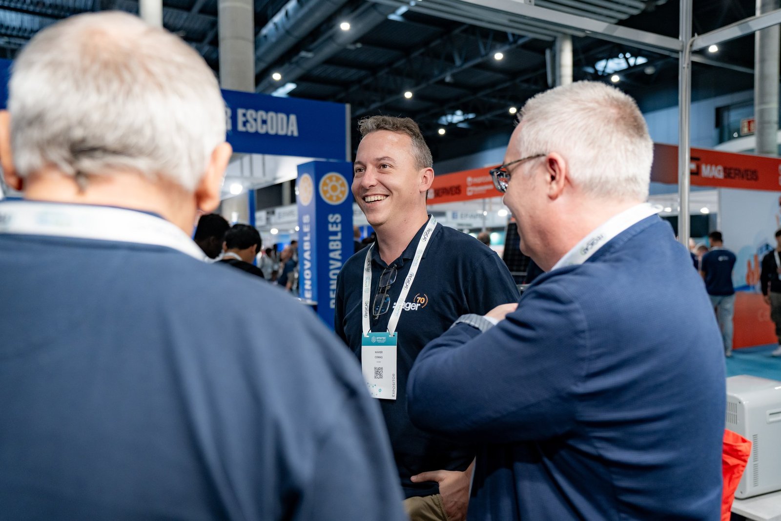 Xavier Comas de Hager sonríe conversando con dos hombres en el evento Efintec. Fondo de stands y carteles.