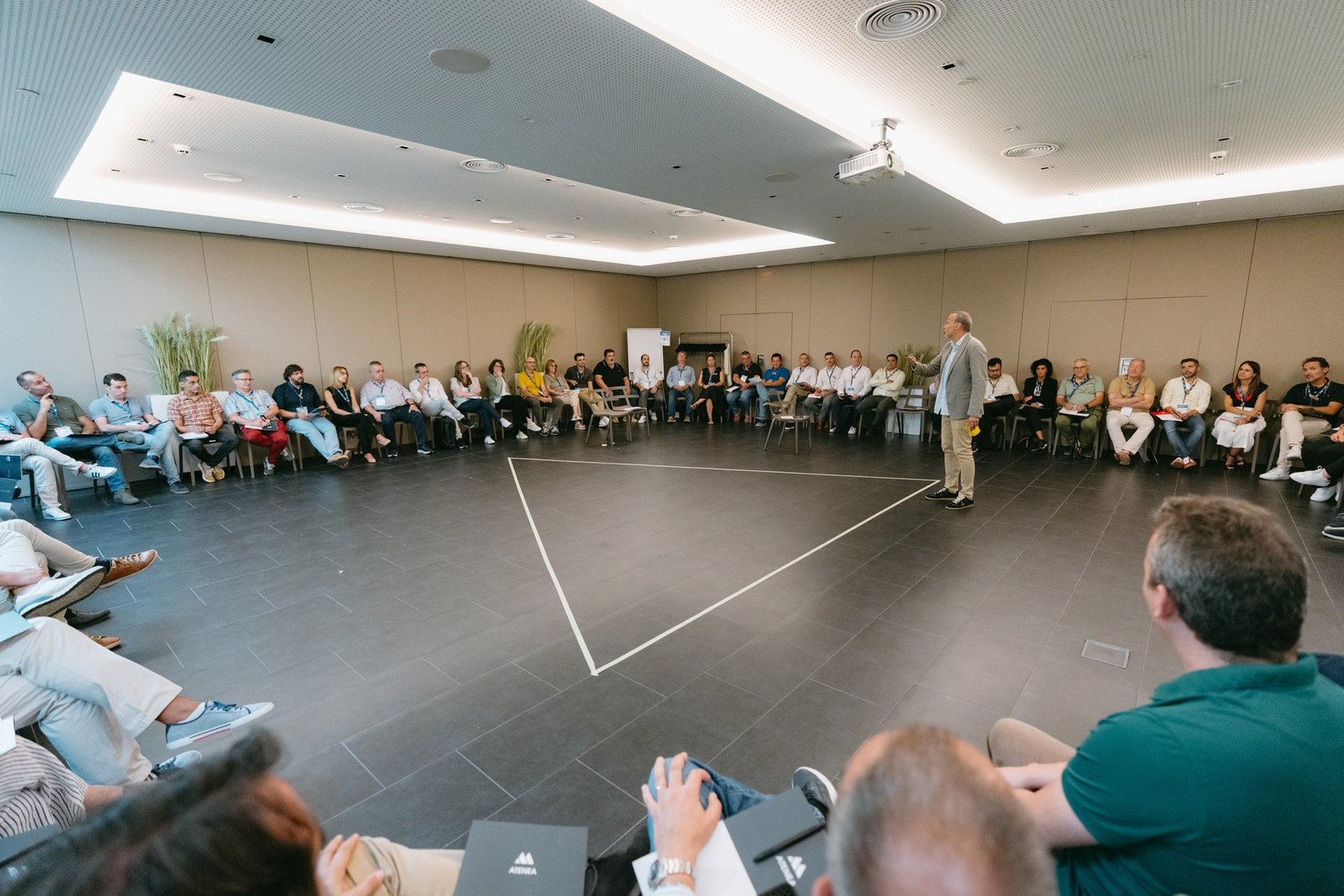 Teambuilding de Hager: Grupo de personas sentadas en círculo en sala moderna. Un orador de pie en el centro interactúa con los participan…