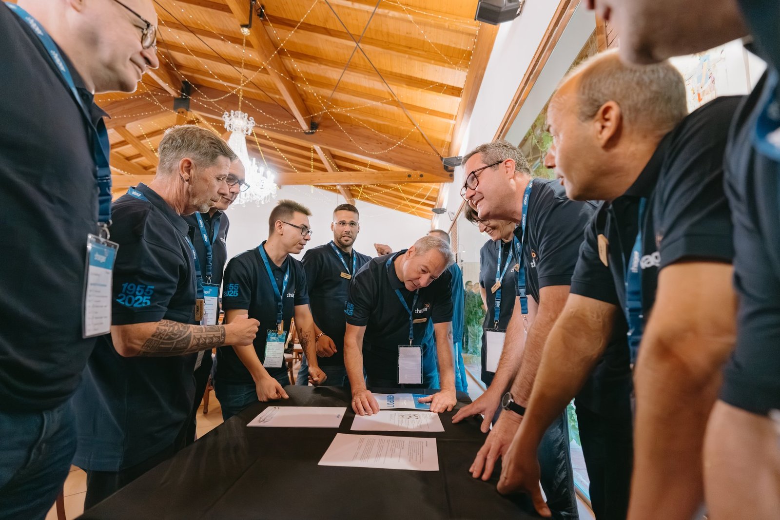 Hombres de Hager en teambuilding, con polos azules, concentrados en documentos sobre una mesa. Ambiente de colaboración.