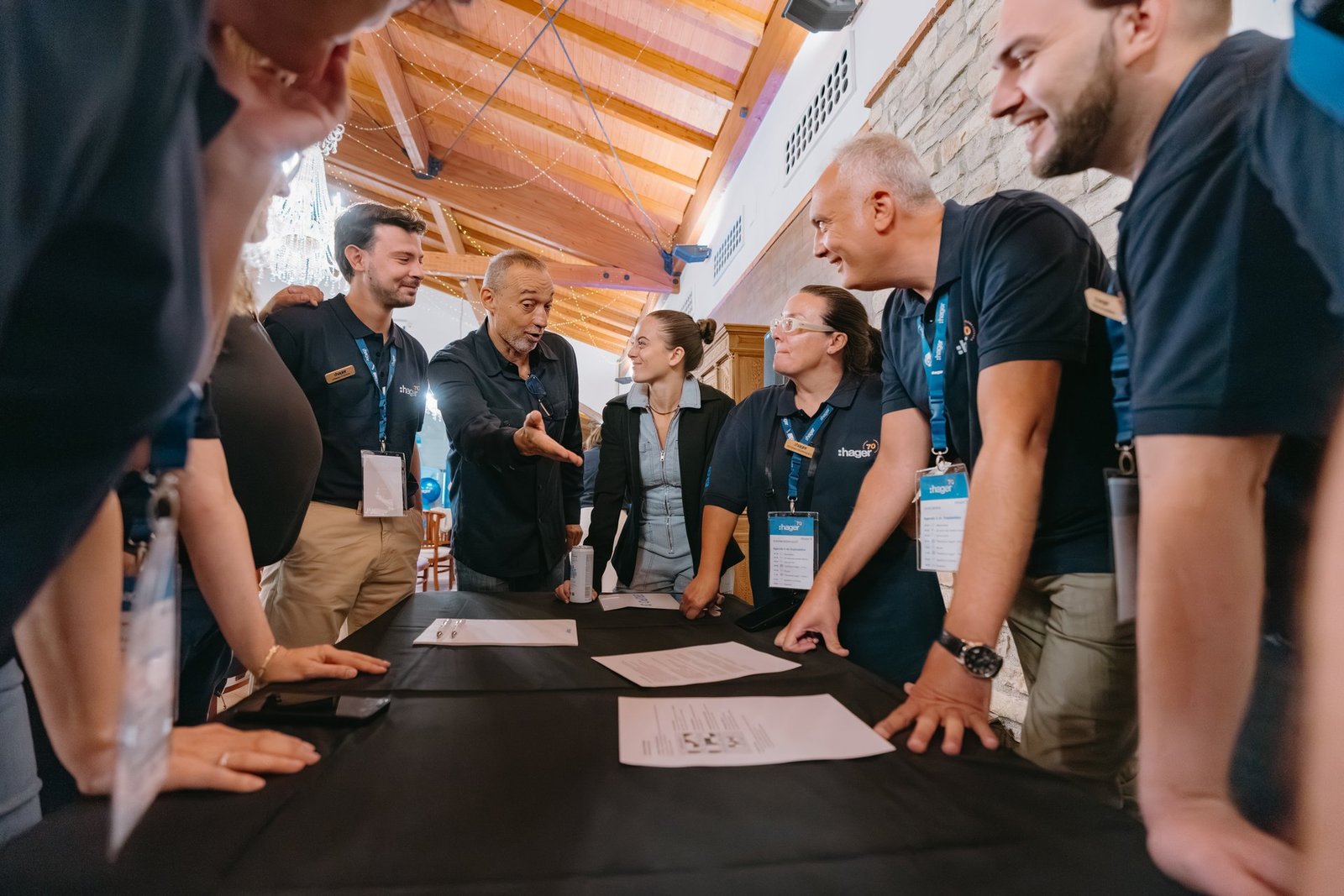 Empleados de Hager en teambuilding. Un hombre gesticula y habla a un grupo que escucha atentamente alrededor de una mesa con documentos.