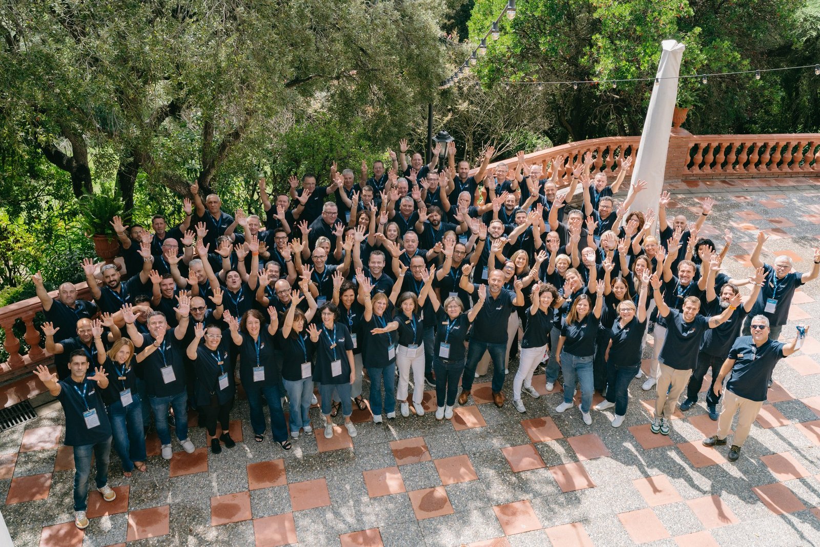 Gran equipo de Hager sonriendo y saludando con las manos en alto en un evento de teambuilding al aire libre.