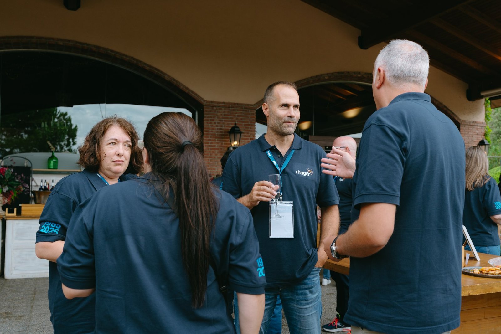 Grupo de empleados de Hager en teambuilding. Un hombre con polo Hager y una mujer con polo 1955-2025 conversan animadamente.