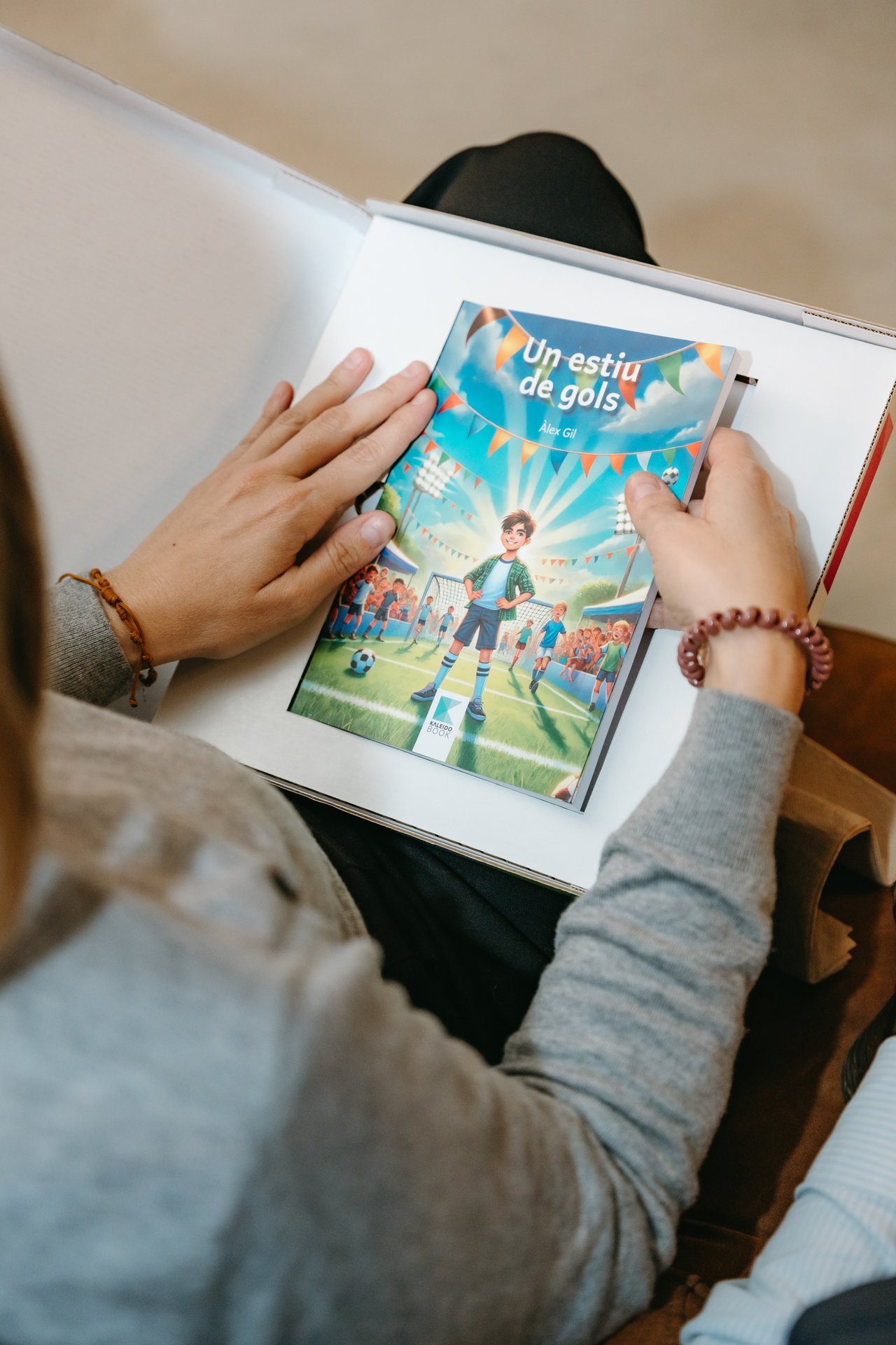 Persona sosteniendo el libro infantil "Un estiu de gols" de KALEIDOBOOK, con un niño en un campo de fútbol en la portada.