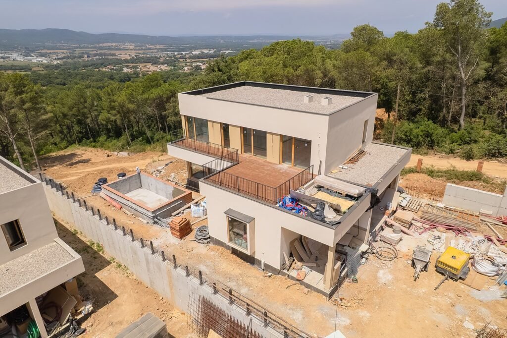 Casa moderna en construcción con piscina, rodeada de obra. Vista aérea de seguimiento de proyecto inmobiliario en entorno natural.