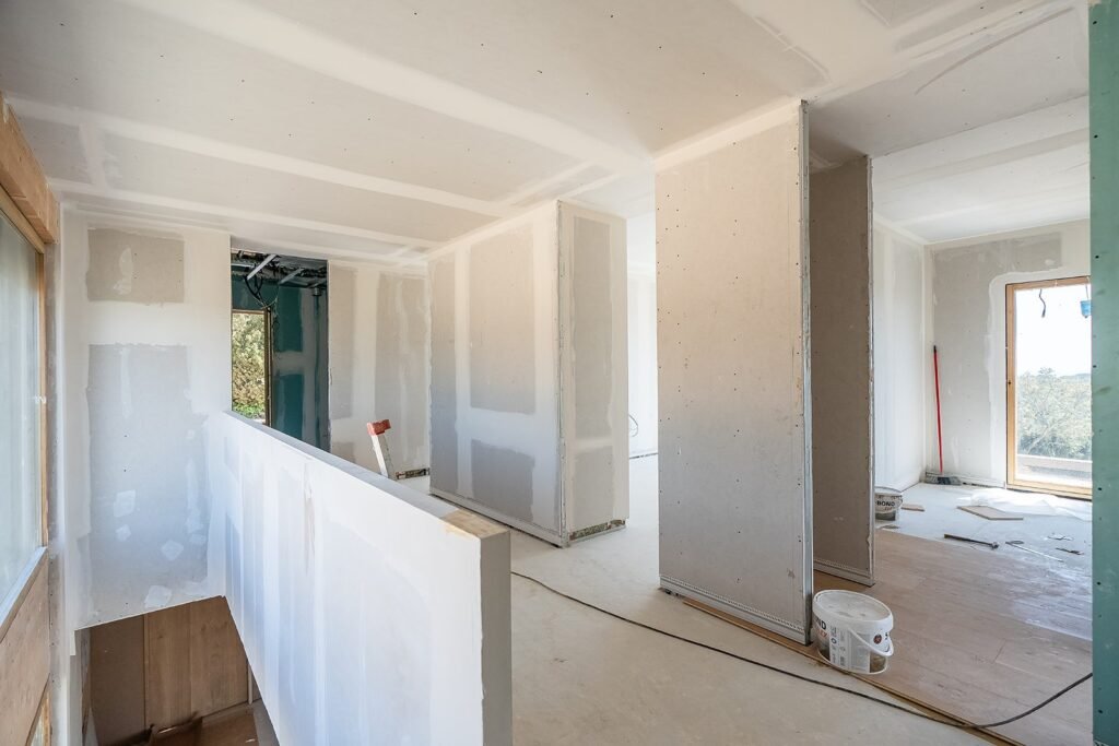 Interior de obra en fase de pladur. Paredes y techos instalados, suelo mixto. Ventanas con vistas al exterior.