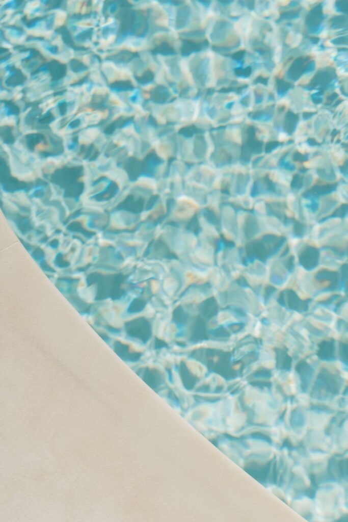 Agua azul turquesa de piscina con reflejos de luz solar y el borde claro de la alberca en primer plano.